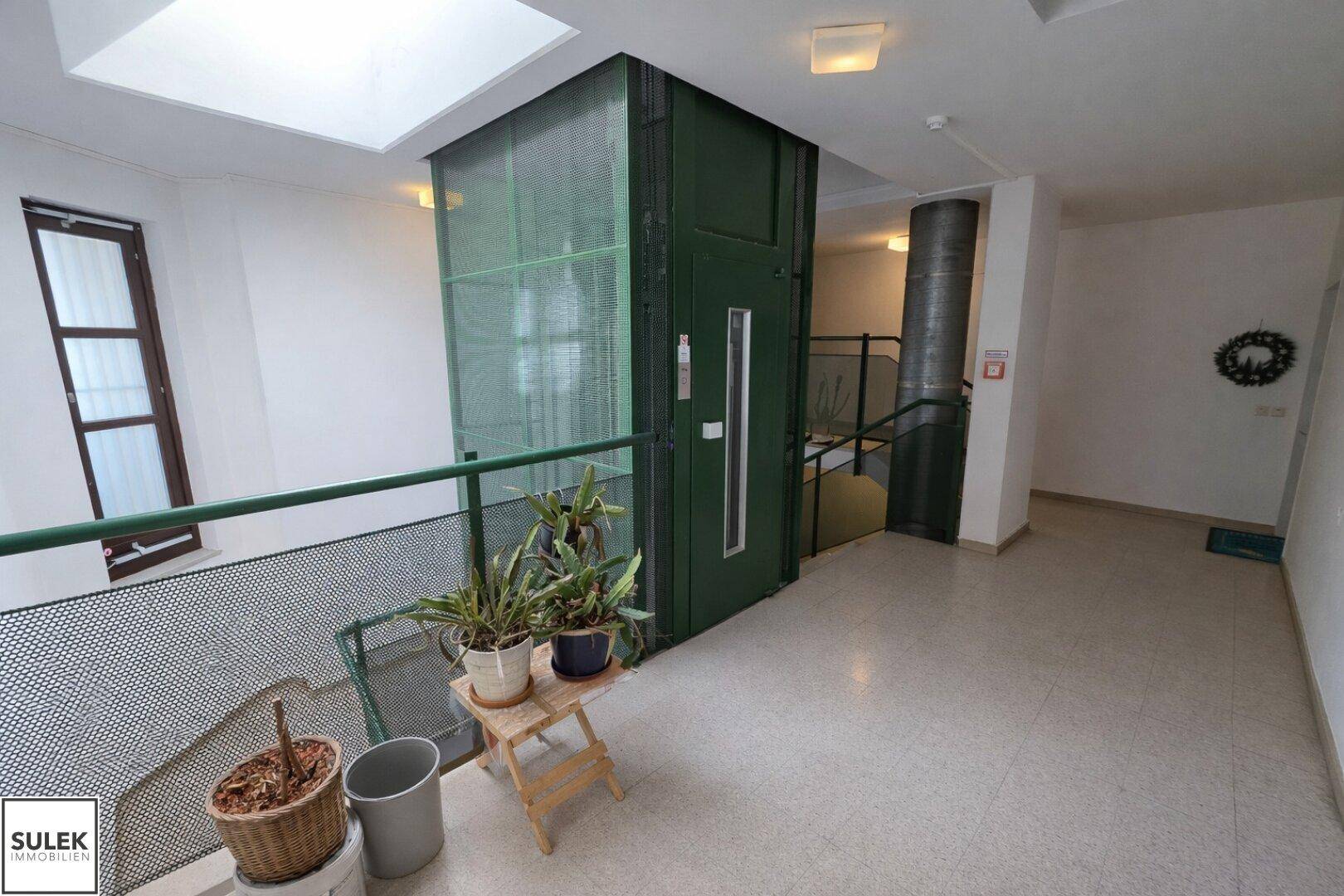 Heller Flur im Gebäude mit Aufzug und Treppenhaus, das zu den Wohnungen führt.