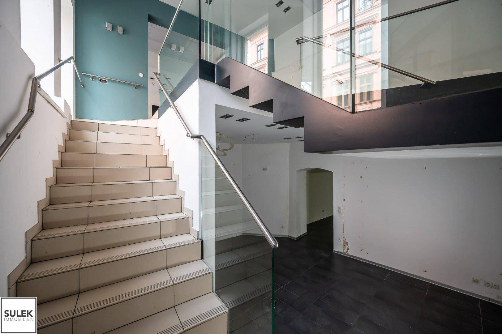 Moderne Treppe mit Glasgeländer und Fliesenstufen, die zu den oberen Etagen führt.