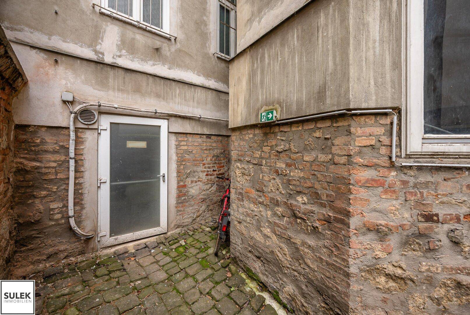 Kleiner Hinterhof mit Ziegelwänden, Kopfsteinpflaster und einer Tür, die zu einem Gebäude führt.