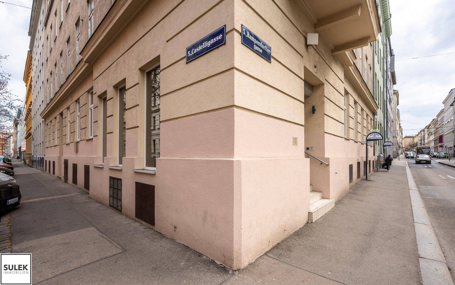 Eckgebäude mit beigefarbener Fassade und Straßenschildern, das den urbanen Charakter unterstreicht.