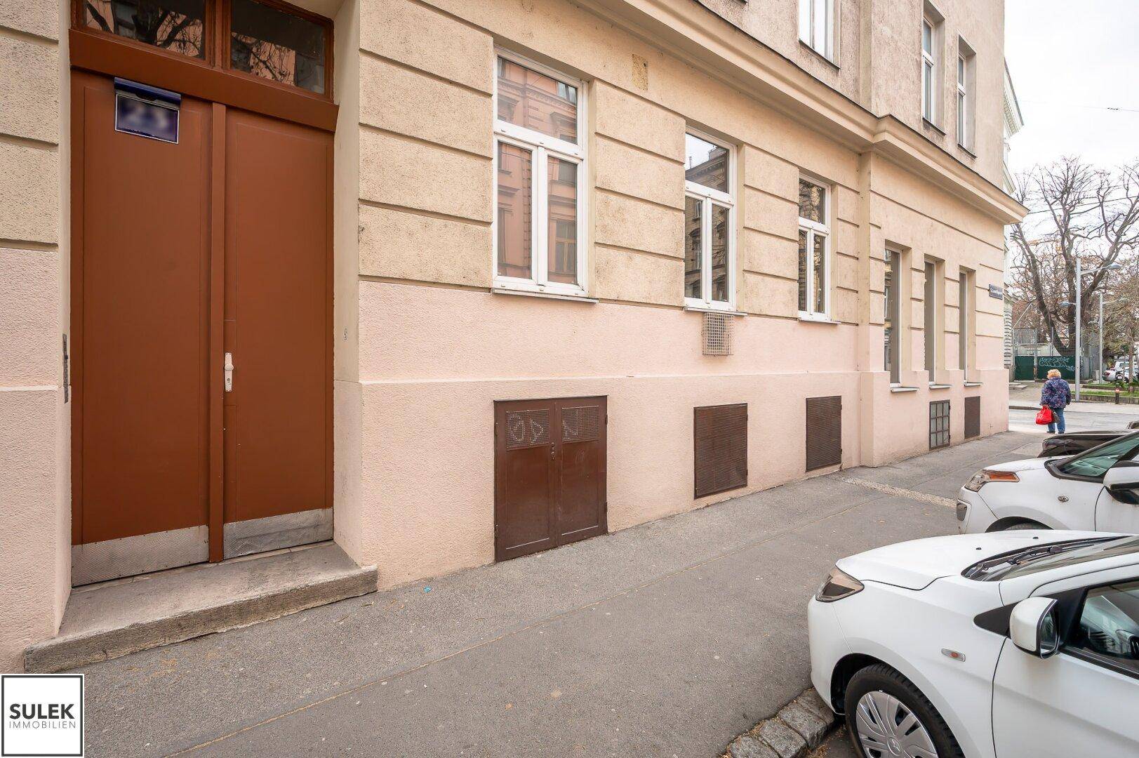 Fassade eines Altbaus mit brauner Eingangstür und Fenstern, die zur Straße zeigen.