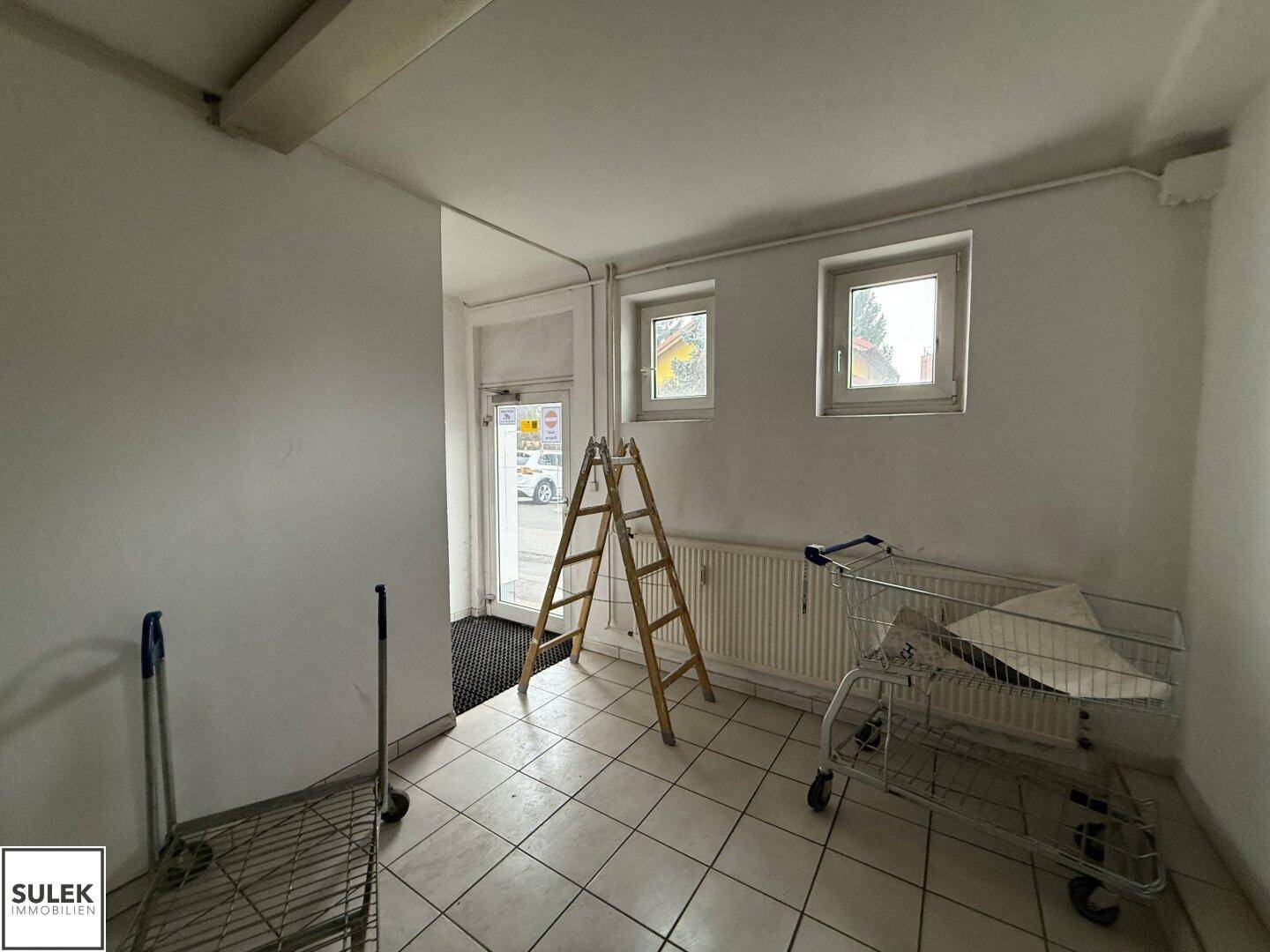 Eingangsbereich mit Fliesenboden, Fenstern und einer Leiter, möglicherweise ein Lagerraum.