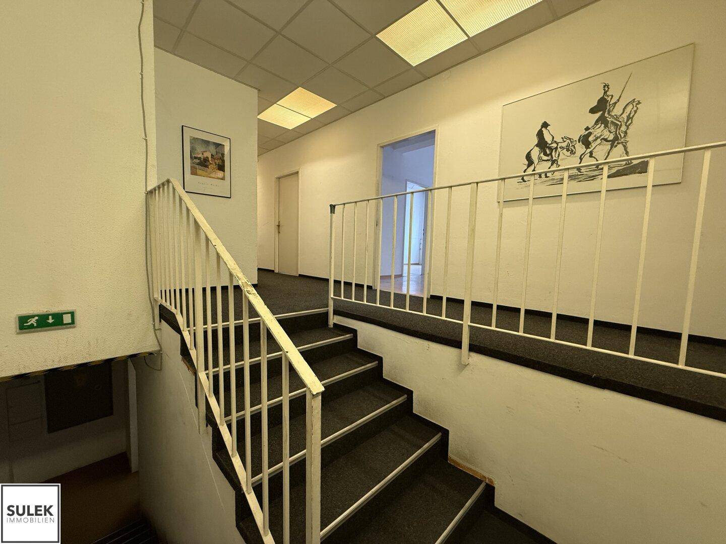Treppenhaus mit Teppichboden und weißem Geländer, das verschiedene Etagen verbindet.