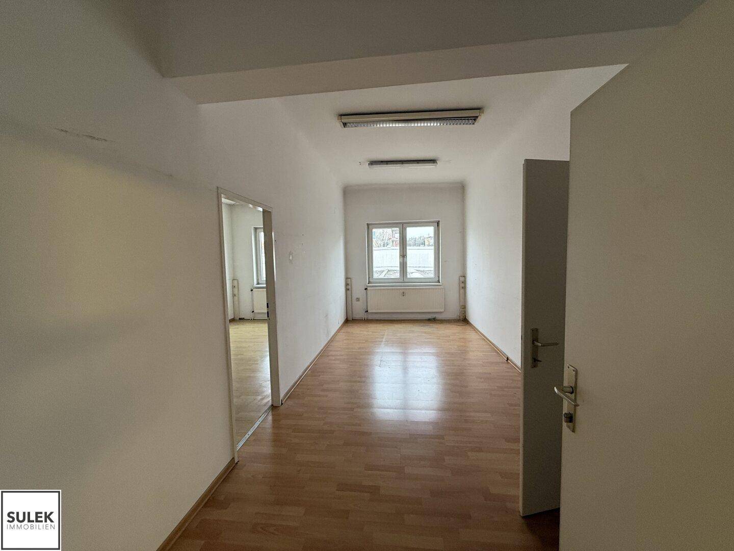 Langer, leerer Büroraum mit Holzboden und Fenstern, der viel Platz bietet.