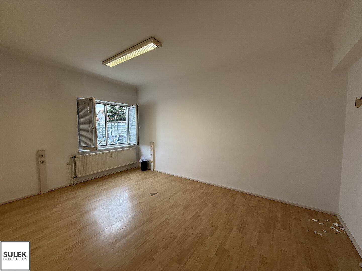 Heller Büroraum mit Holzboden und einem Fenster, das einen Blick nach draußen bietet.