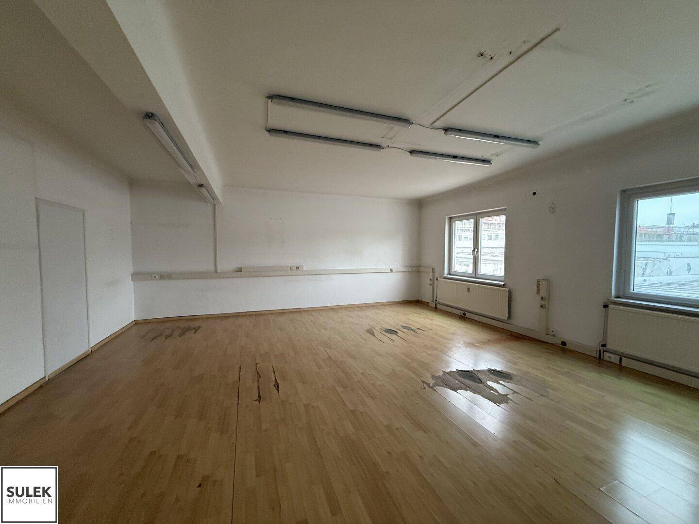 Heller Büroraum mit Holzboden und Tageslicht, ideal für verschiedene Geschäftsnutzungen.