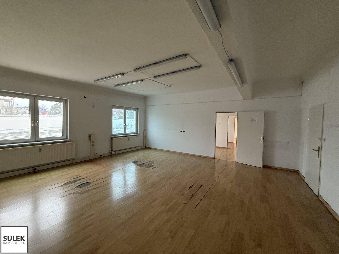 Geräumiger, leerer Büroraum mit Holzboden und großen Fenstern, bereit zur individuellen Gestaltung.