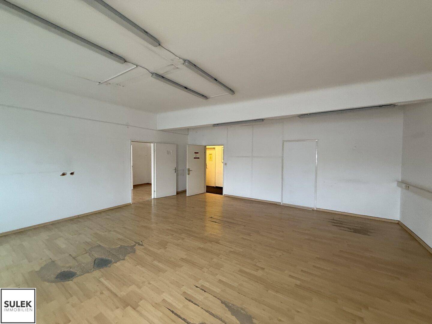 Großer, leerer Büroraum mit Holzboden und Fenstern, bereit zur Neugestaltung.