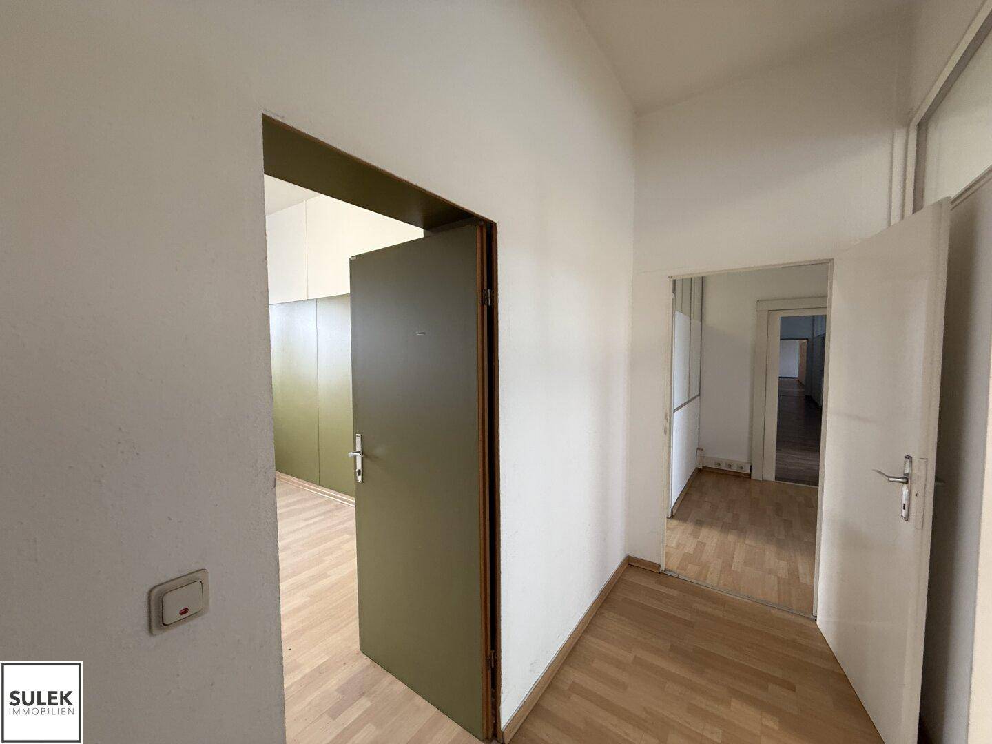Flur mit Laminatboden und mehreren Türen, die zu den angrenzenden Büroräumen führen.