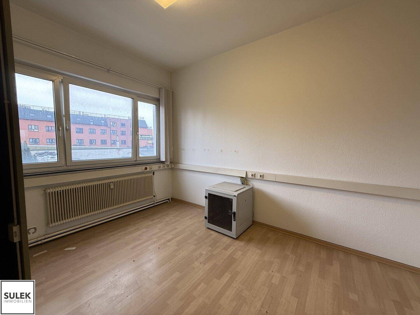 Kleiner Büroraum mit Laminatboden, Fenster und einem Serverschrank an der Wand.