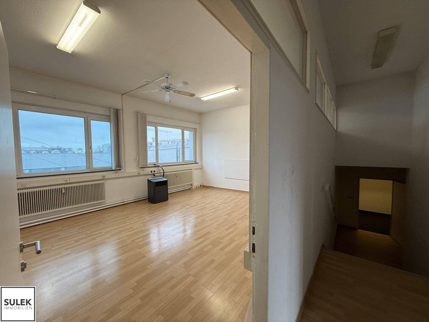 Heller Büroraum mit Laminatboden, großen Fenstern und einem Blick auf die Umgebung.