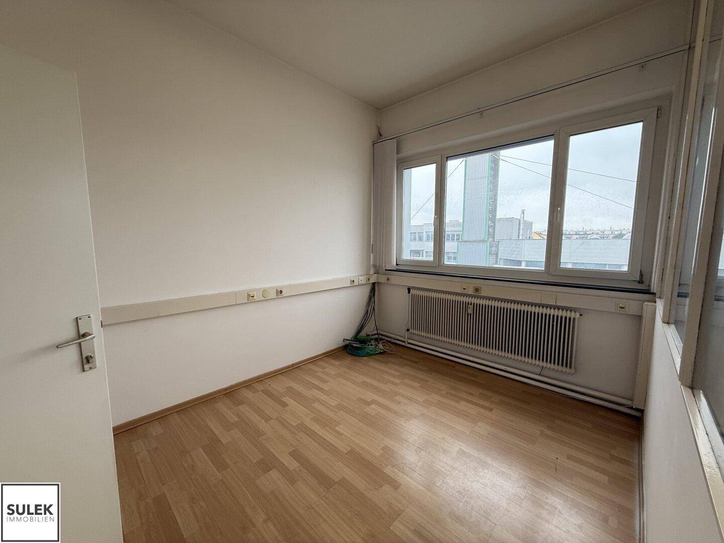 Kleiner Büroraum mit Laminatboden, Fenster und Heizkörper, ideal für Einzelarbeitsplätze.
