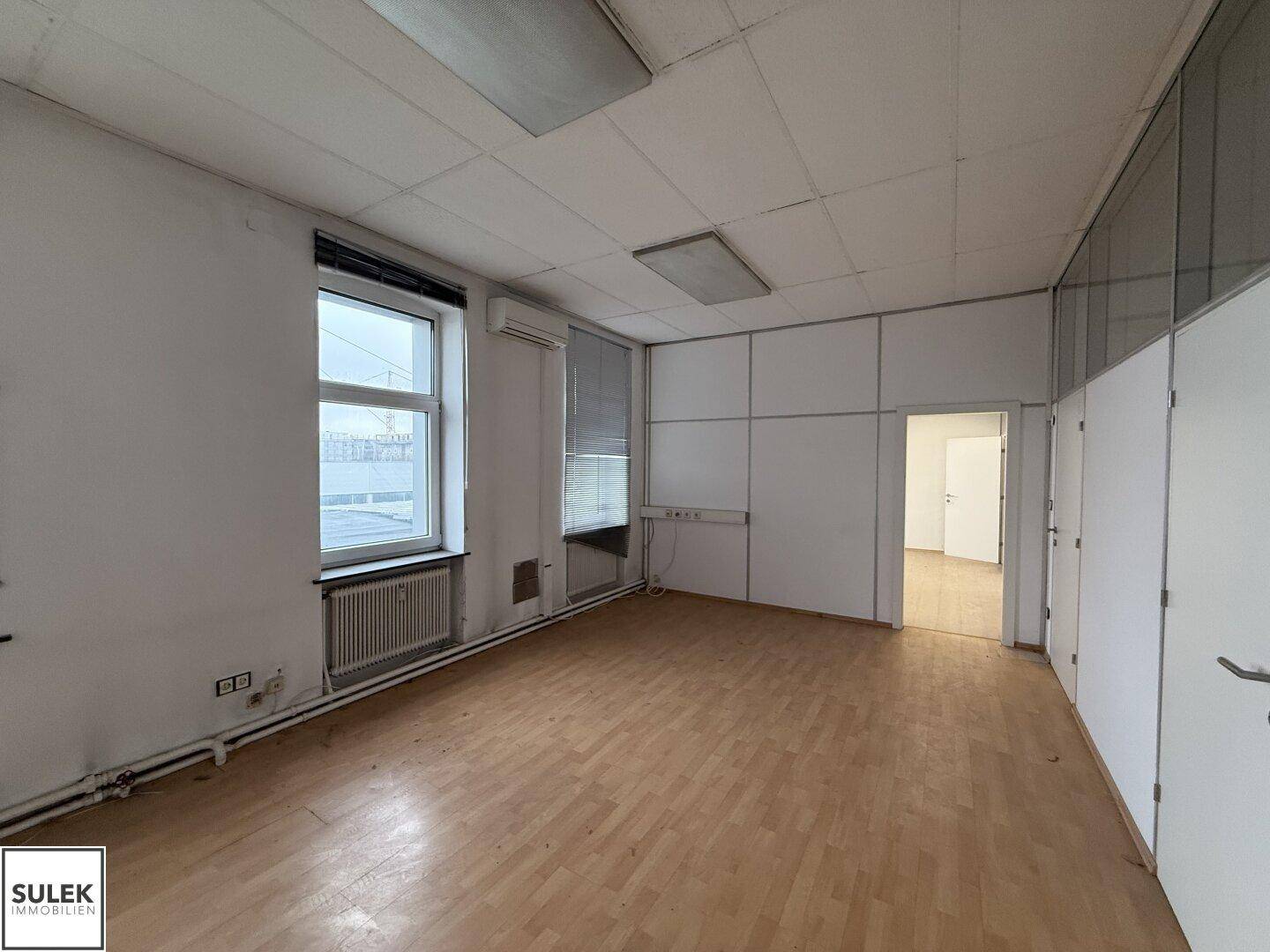 Büroraum mit Laminatboden, Fenstern und Klimaanlage, bereit für die Einrichtung.