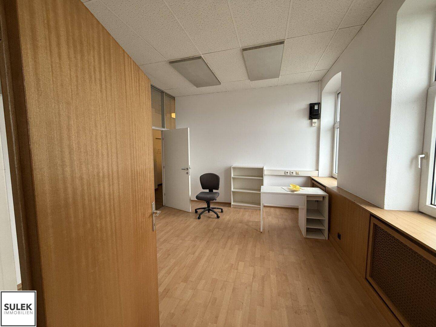 Büroraum mit Holzboden, Fenster und Büromöbeln, bereit zur Nutzung.