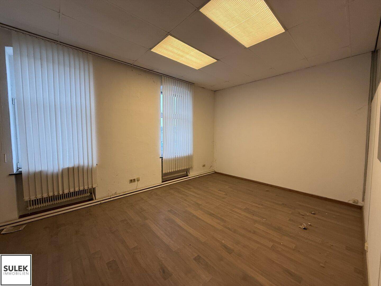Büroraum mit Holzboden, Fenstern und Jalousien, bereit zur Einrichtung.