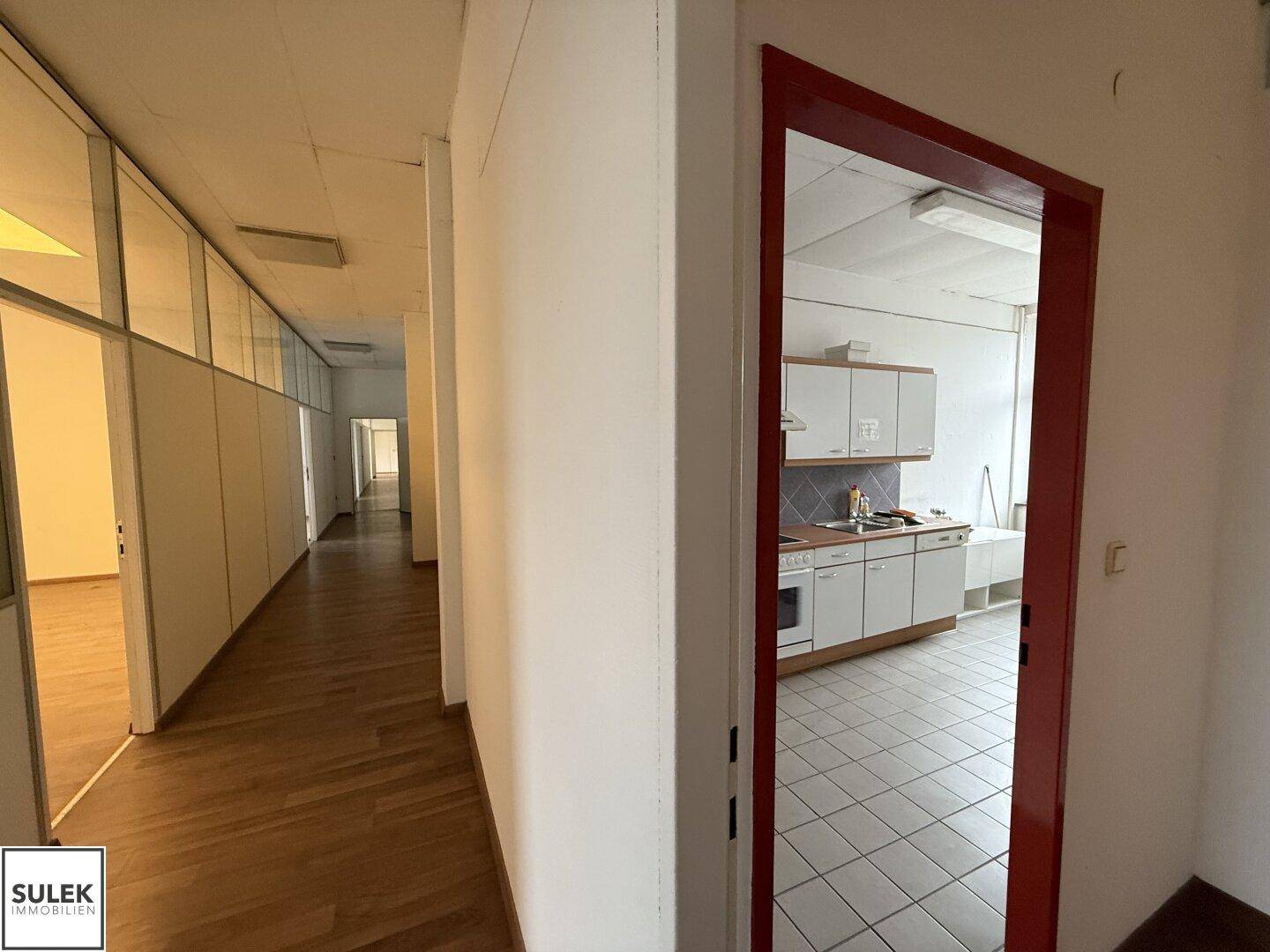 Flur mit Holzboden und einem Blick in eine angrenzende Küche mit weißen Schränken.