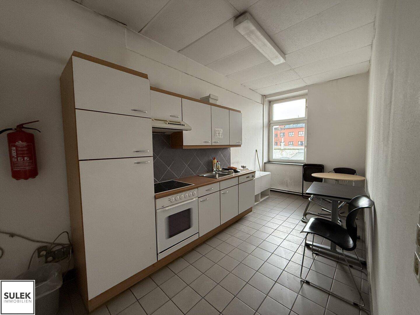 Einfache Küche mit weißen Schränken, Fliesenboden und einem Fenster, ideal für Mitarbeiter.