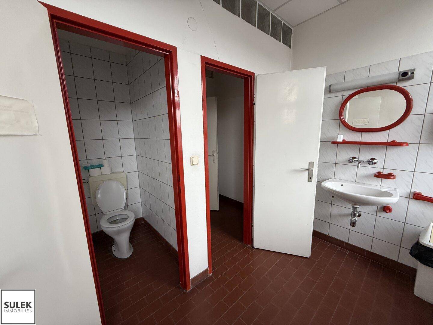 Badezimmer mit roten Fliesen, weißen Wandfliesen und zwei separaten Toilettenbereichen.
