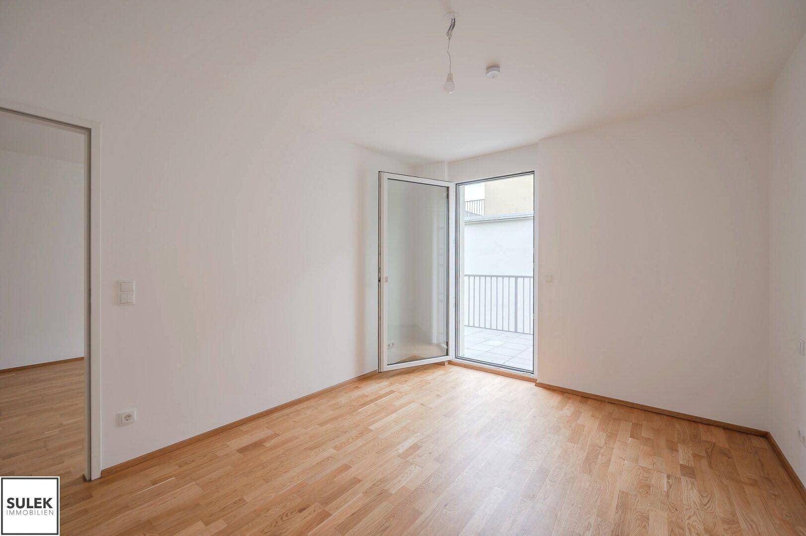 Helles Schlafzimmer mit Parkettboden und einer Tür, die zu einem Außenbereich führt.