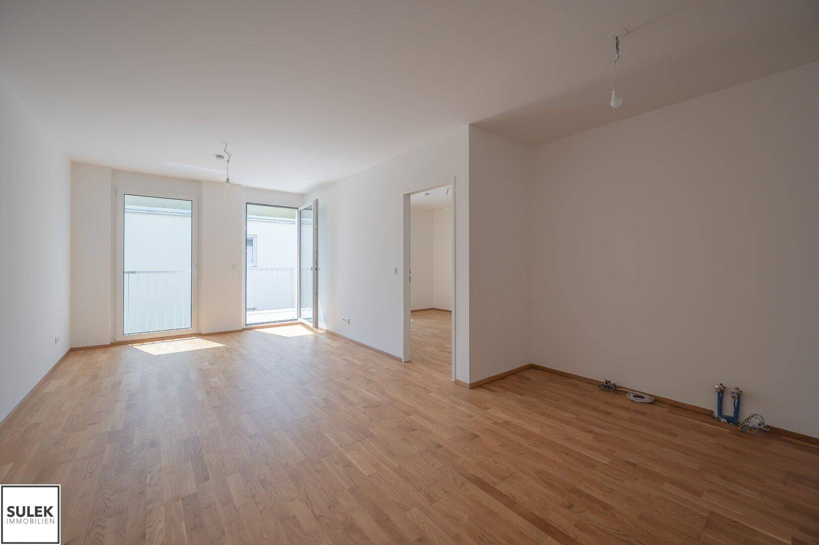 Geräumiger, heller Wohnbereich mit Parkettboden und großen Fenstern zum Balkon.