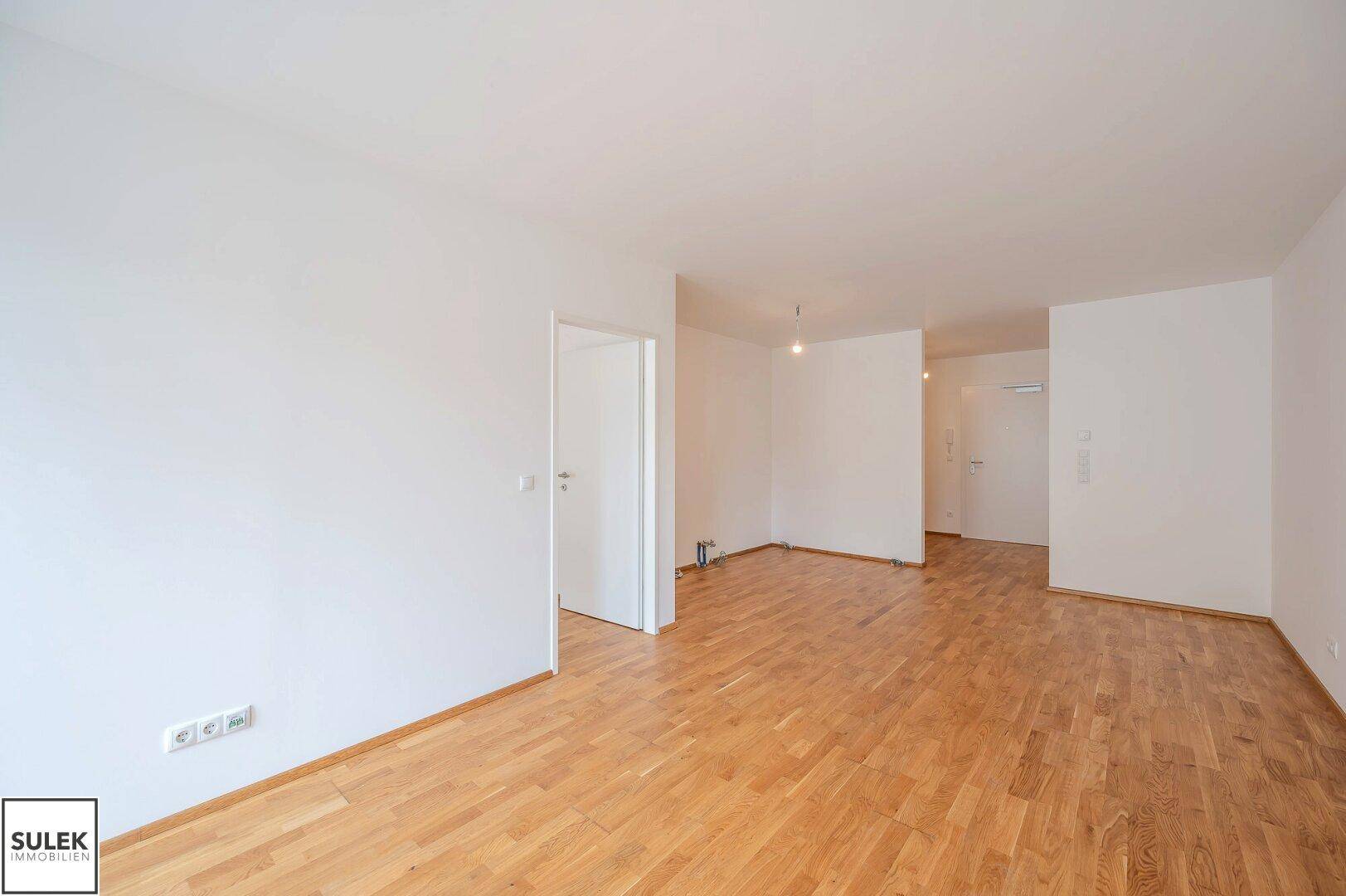 Leerer Innenraum mit Parkettboden und weißen Wänden, bereit für die Einrichtung.