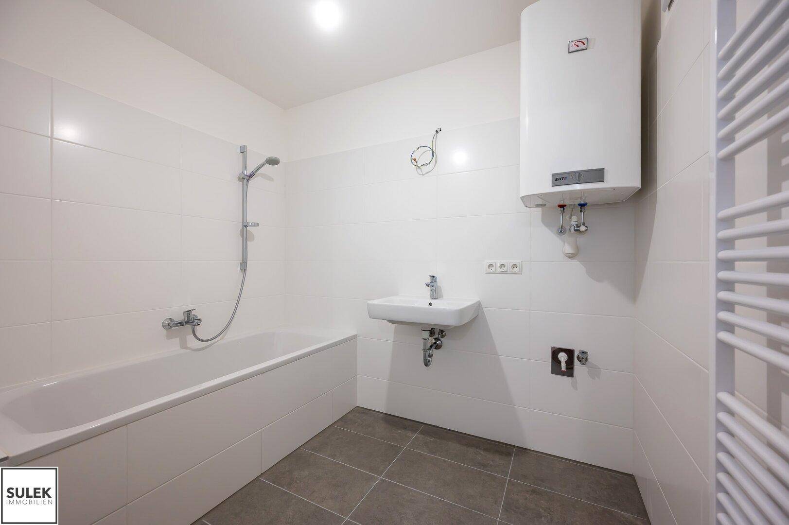 Modernes Badezimmer mit Badewanne, Waschbecken, Wandfliesen und Warmwasserboiler.