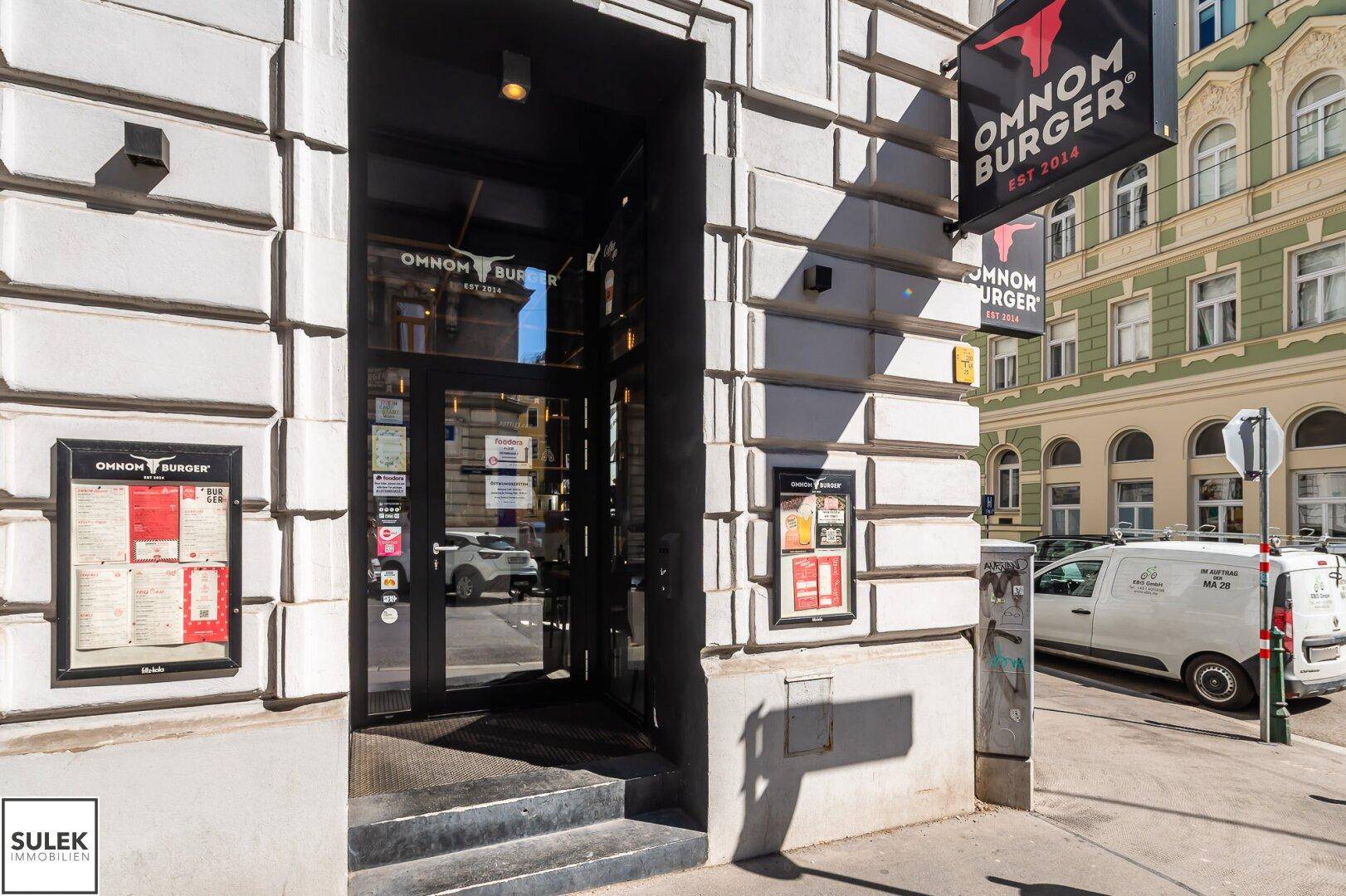 Eingangsbereich eines Restaurants in einem historischen Gebäude mit Werbeschildern und Blick auf die Straße.