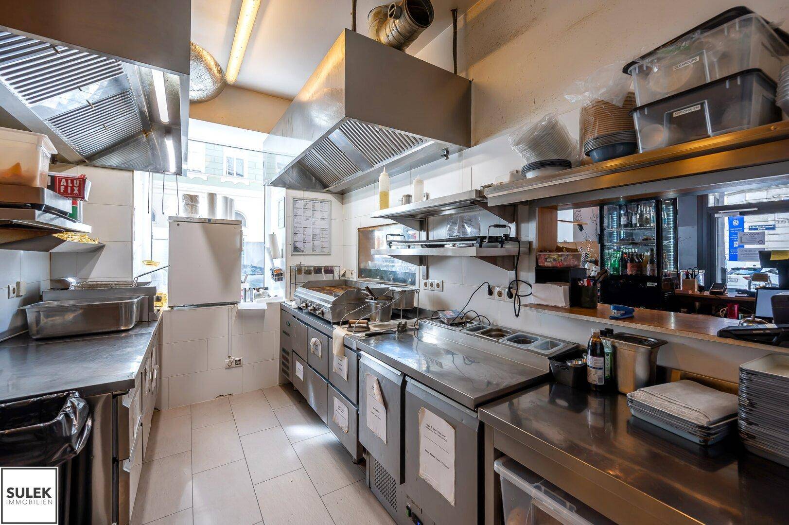 Professionelle Restaurantküche mit Edelstahlgeräten, Dunstabzugshaube und Arbeitsflächen, bereit für den Betrieb.