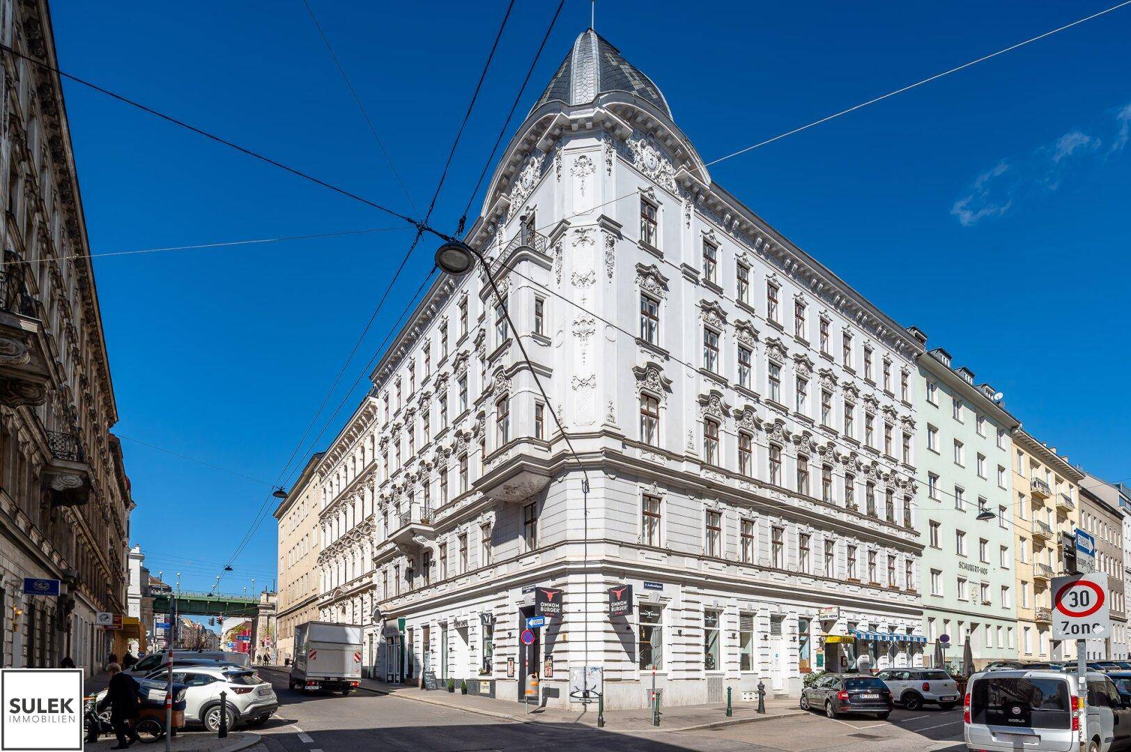 Historisches Eckgebäude mit markanter Architektur und Geschäften im Erdgeschoss an einer belebten Straße.