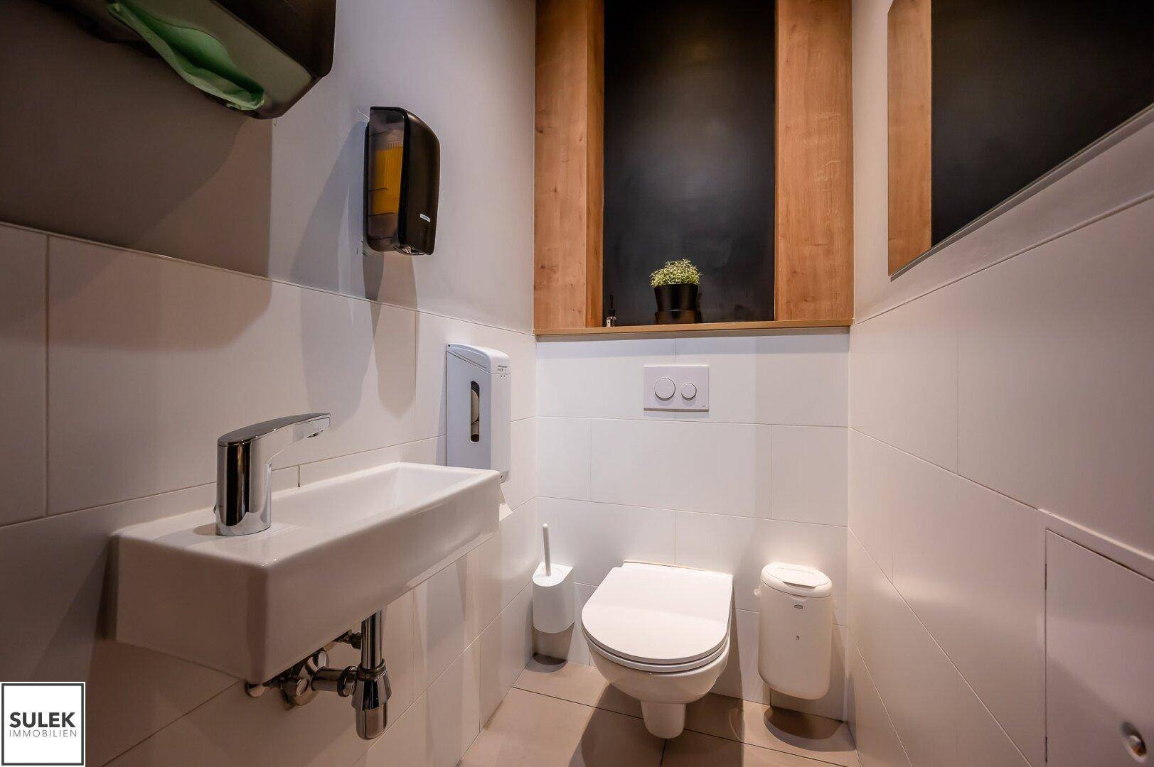 Modernes Gäste-WC mit wandhängender Toilette, kleinem Waschbecken und weißen Fliesen.
