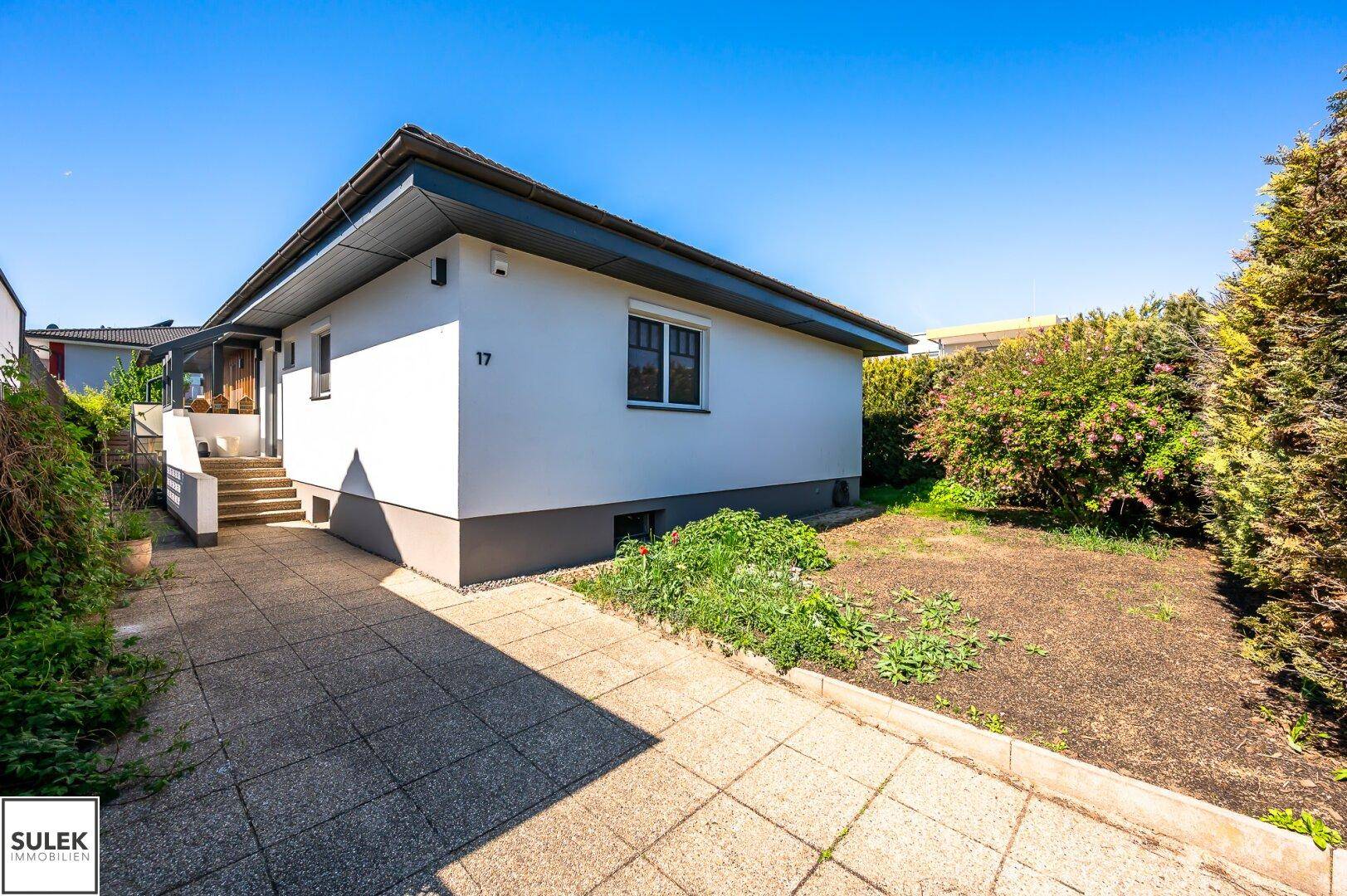 Seitenansicht des Hauses mit gepflasterter Auffahrt und einem Bereich für Gartengestaltung.