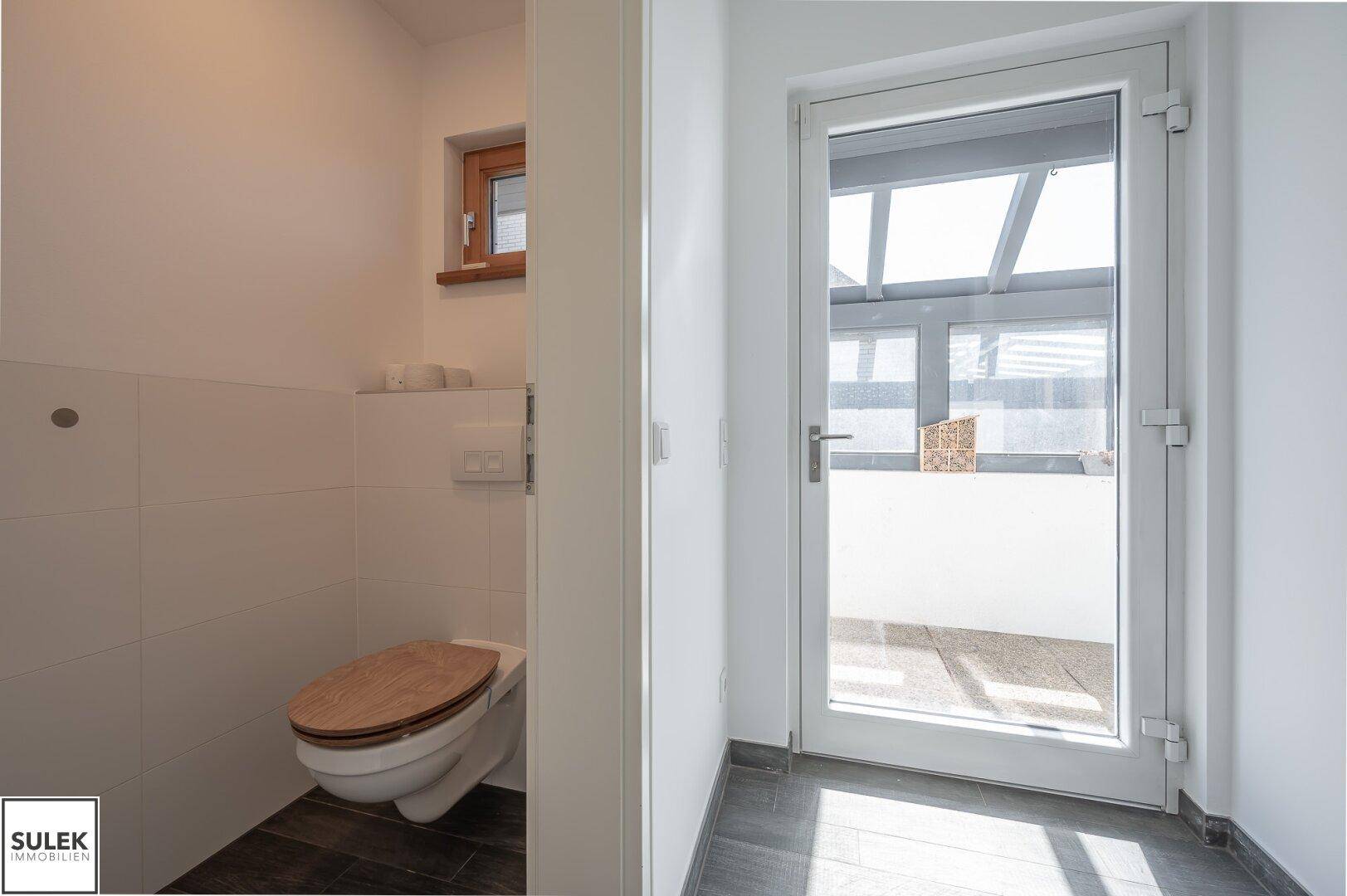 Modernes Gäste-WC mit wandhängender Toilette, kleinem Fenster und Zugang zum Außenbereich.