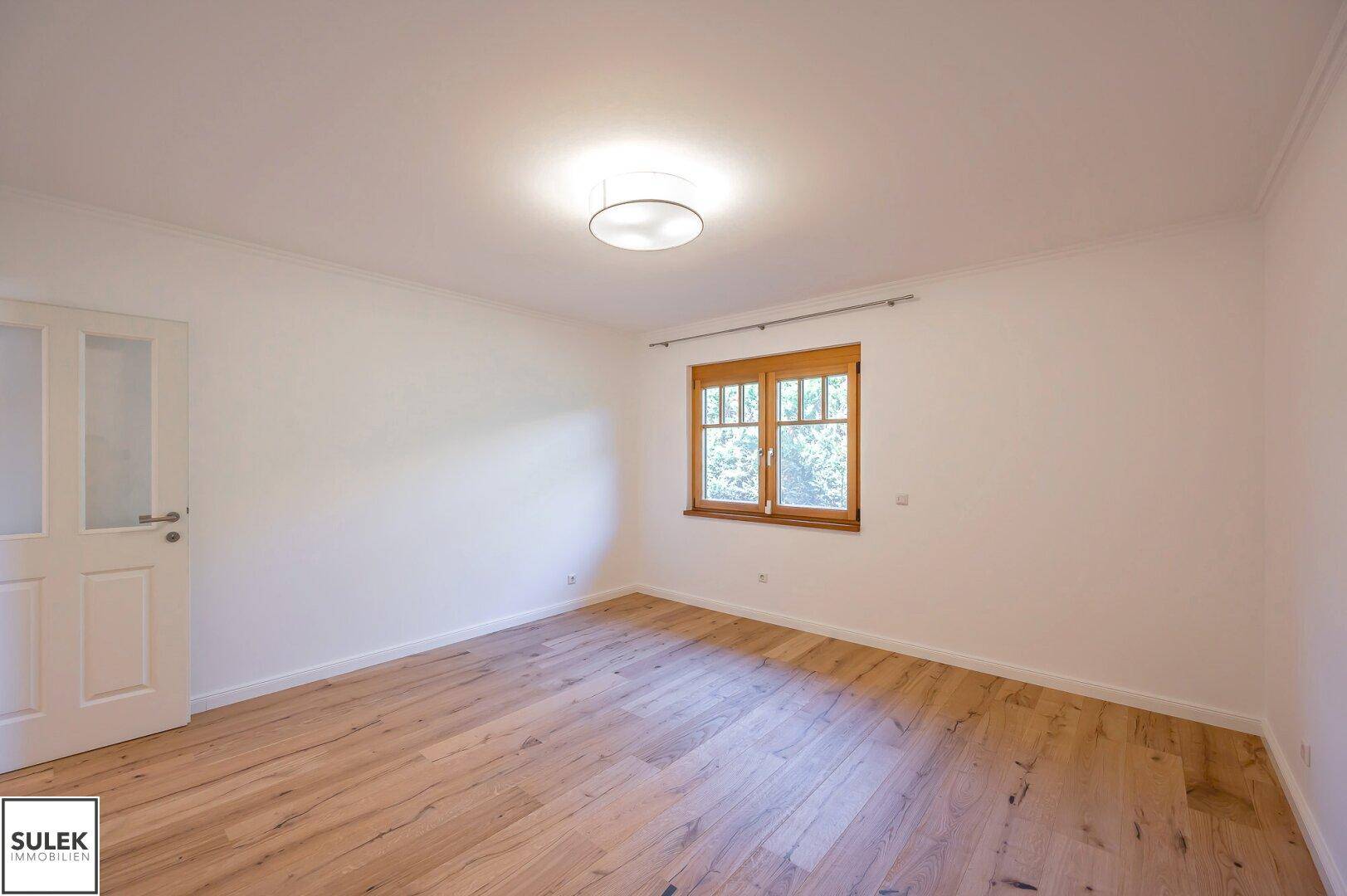 Geräumiges Schlafzimmer mit Holzboden und einem großen Fenster, das viel Tageslicht hereinlässt.