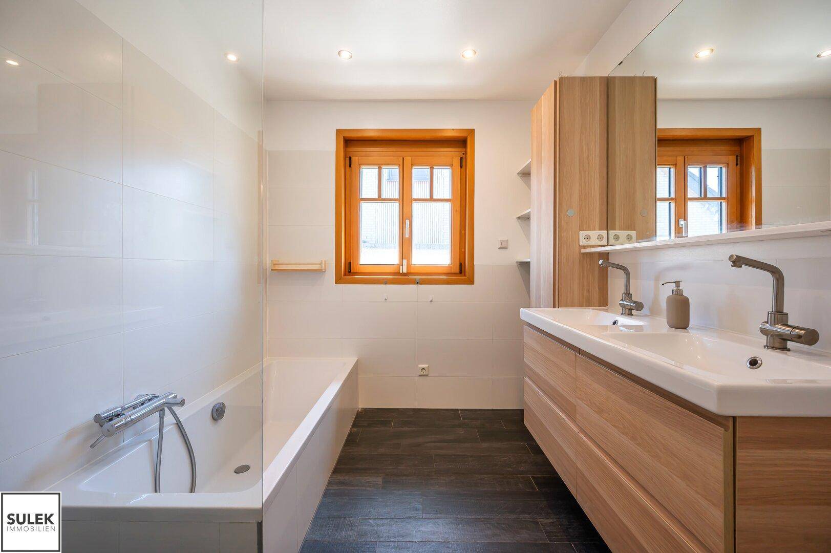 Modernes Badezimmer mit Doppelwaschbecken, Badewanne und einem Fenster für natürliche Belüftung.
