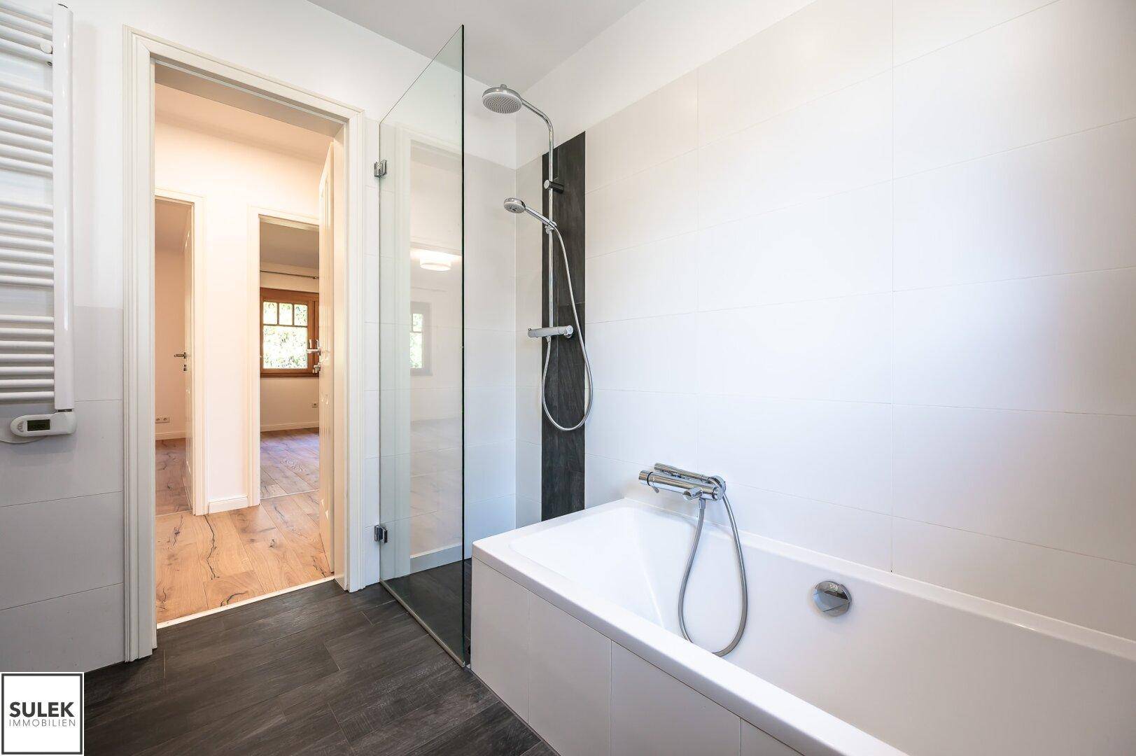Badezimmer mit Badewanne, integrierter Dusche und einem beheizten Handtuchhalter für zusätzlichen Komfort.