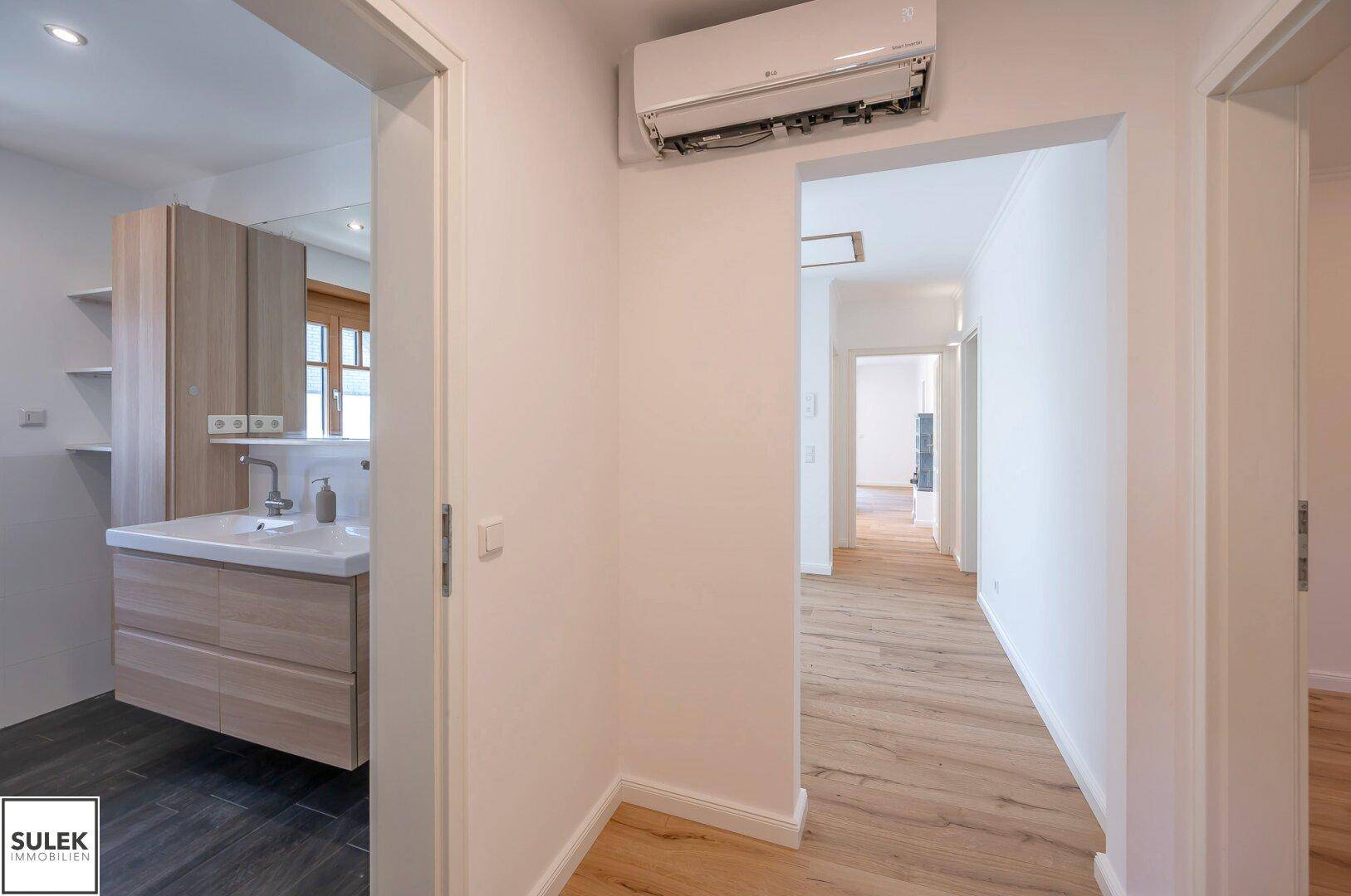 Heller Flur mit Holzboden, Klimaanlage und direktem Zugang zu einem modernen Badezimmer.