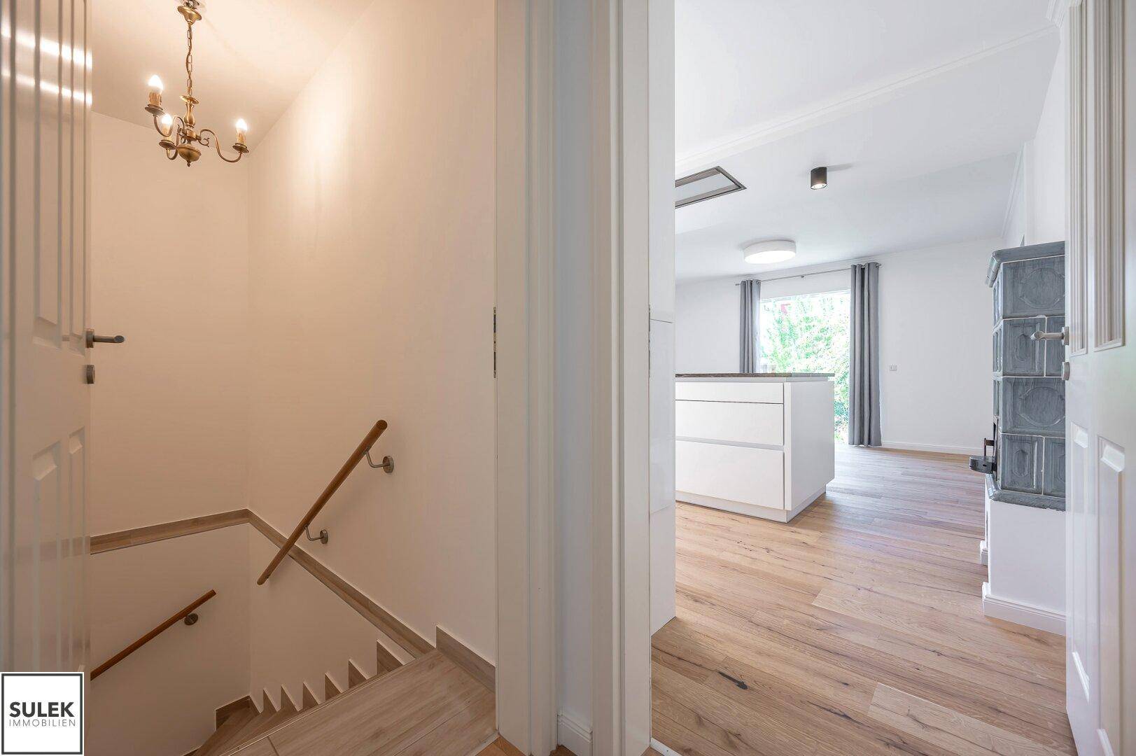 Holztreppe mit Handlauf, die in das Untergeschoss führt, mit Blick auf den Wohnbereich im Hintergrund.