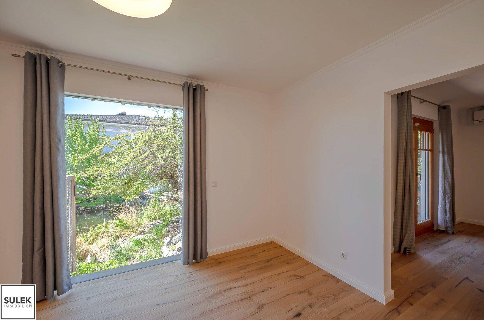 Heller Raum mit großem Fenster, das einen direkten Blick auf den Teich und die grüne Umgebung bietet.
