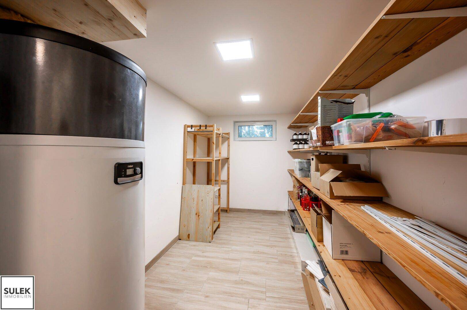 Geräumiger Hauswirtschaftsraum mit Warmwasserspeicher, Holzregalen und kleinem Fenster.
