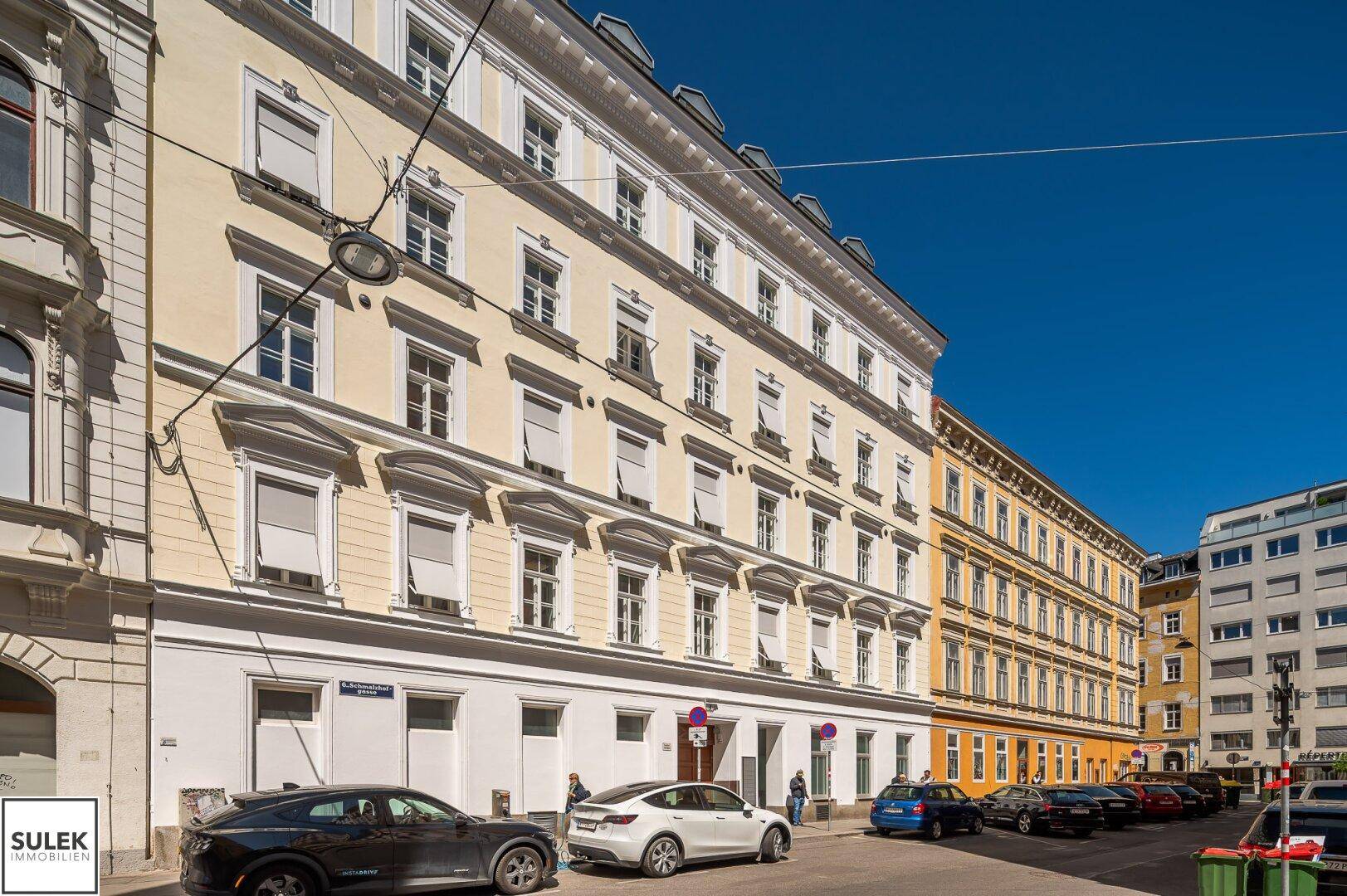 Historisches Gebäude mit gelber Fassade und vielen Fenstern, an einer belebten Stadtstraße gelegen.