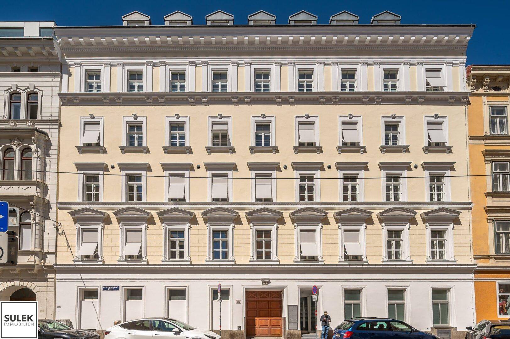 Historisches Gebäude mit gelber Fassade und vielen Fenstern, an einer belebten Stadtstraße gelegen.