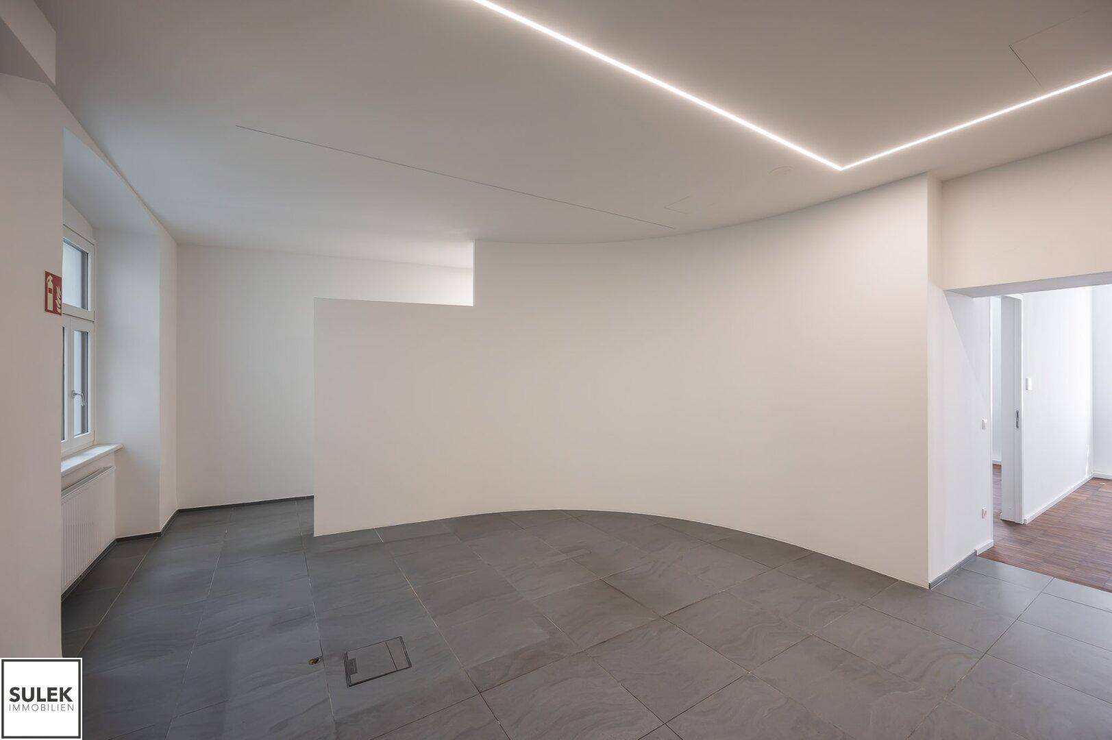 Geräumiger Bürobereich mit Fliesenboden und geschwungener Wand, ideal für eine moderne Arbeitsumgebung mit viel Platz.