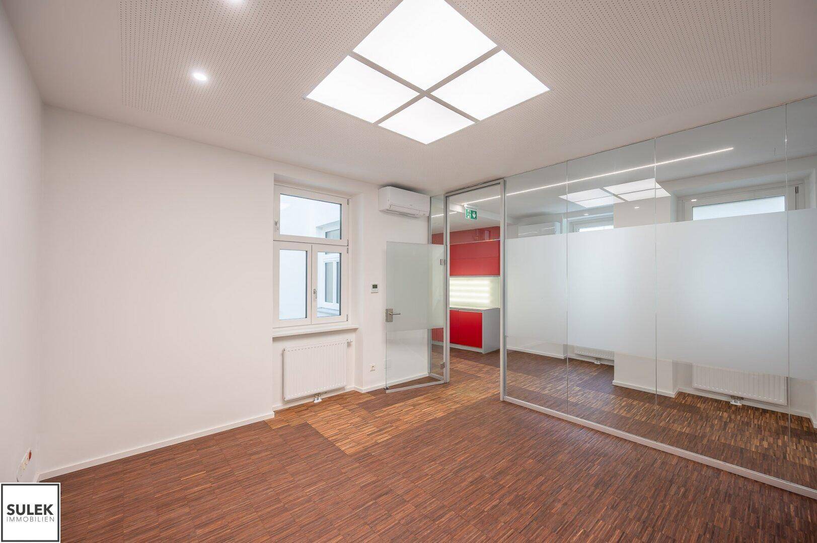 Modernes Büro mit Holzboden und Glaswänden, bietet eine helle und offene Arbeitsumgebung mit viel Tageslicht.