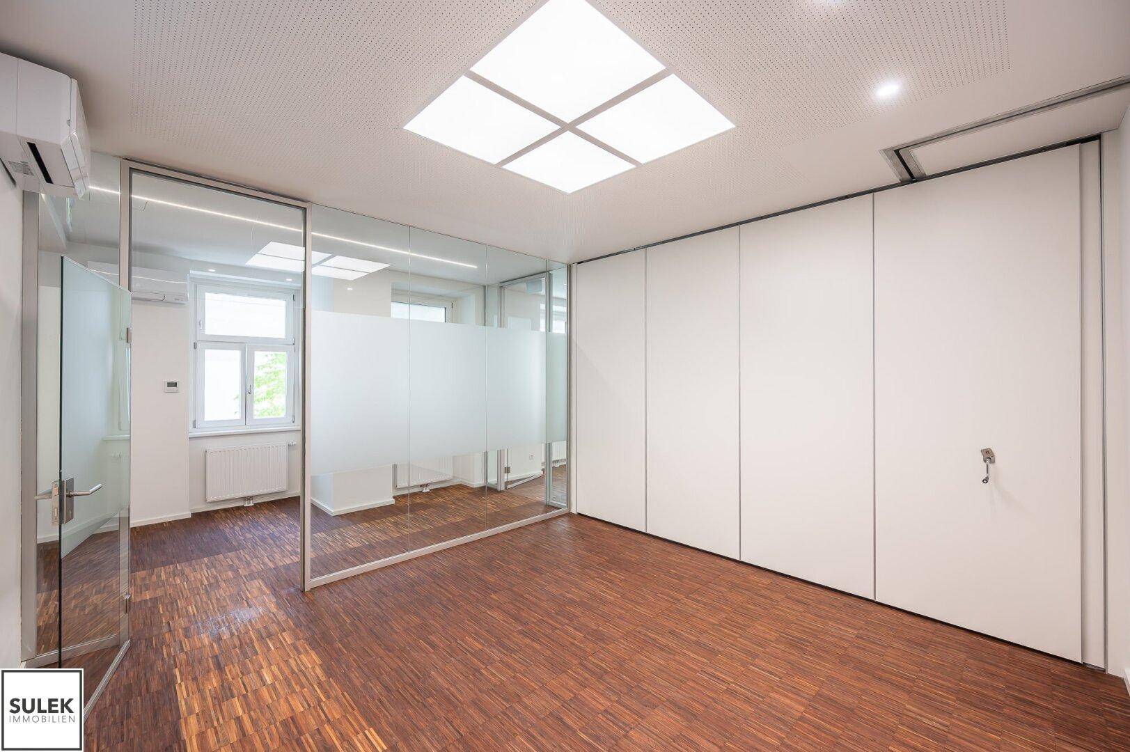 Geräumiges Büro mit Holzboden und Glaswänden, die eine flexible Raumgestaltung ermöglichen und viel Licht spenden.