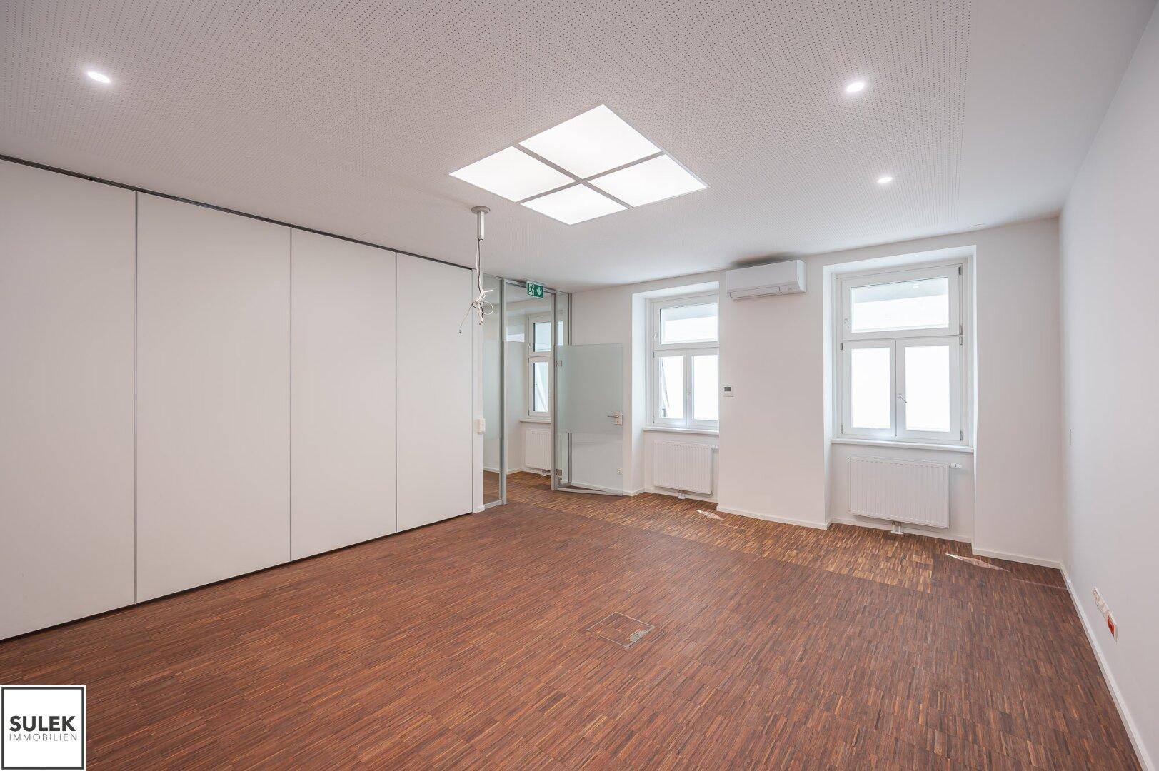 Helles Büro mit Holzboden, Einbauschränken und großen Fenstern, ideal für konzentriertes Arbeiten und viel Tageslicht.