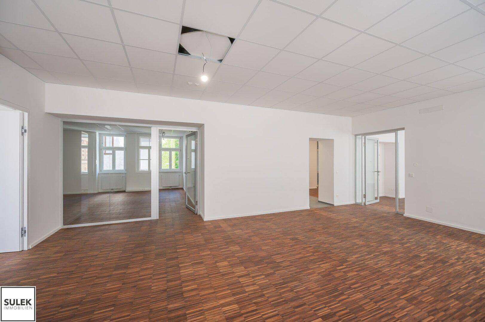 Großzügiges Büro mit Holzboden und Glaswänden, die eine offene und flexible Raumgestaltung ermöglichen.