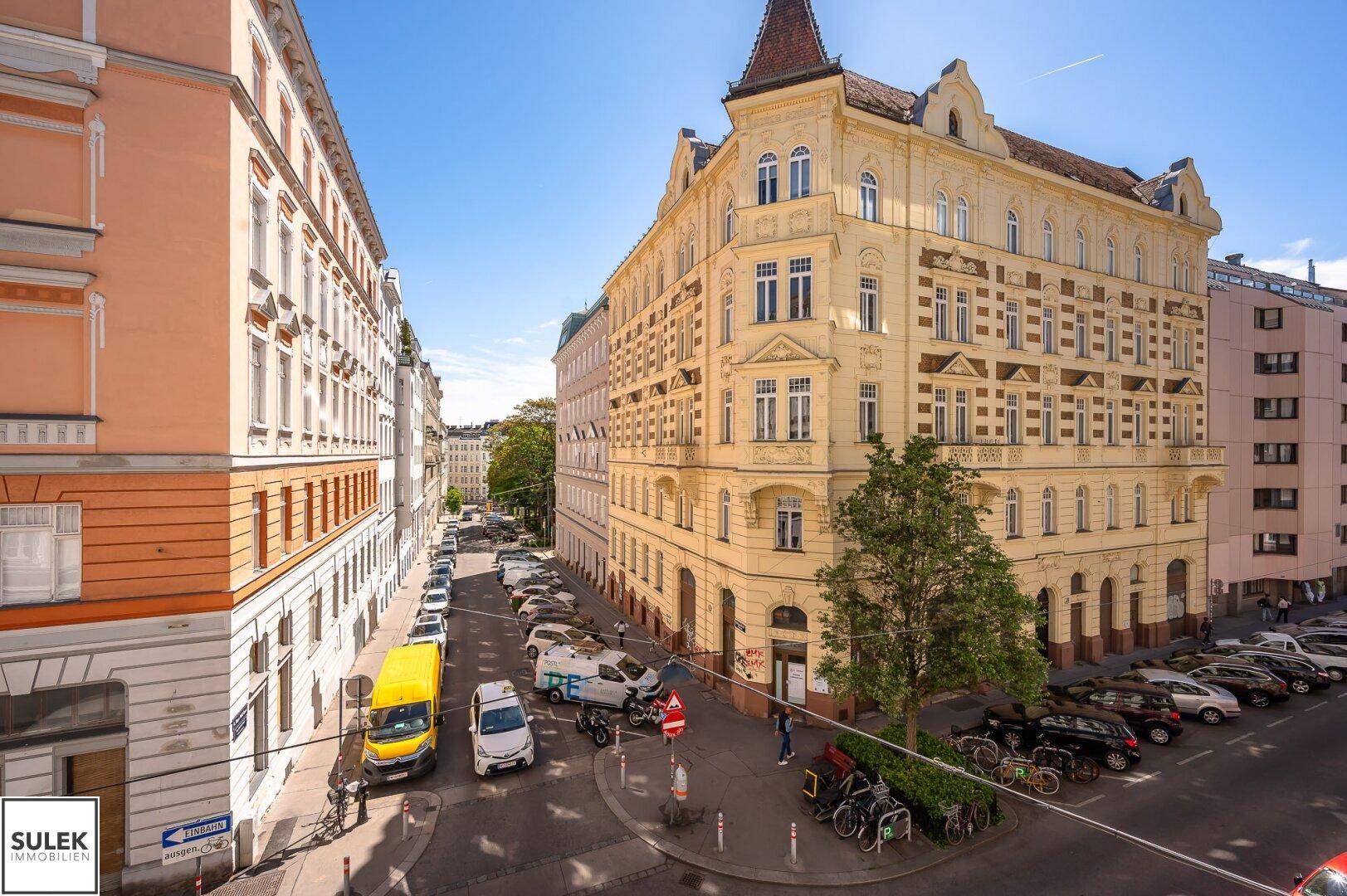 Historisches Eckgebäude mit gelber Fassade und vielen Fenstern, an einer belebten Stadtkreuzung gelegen.