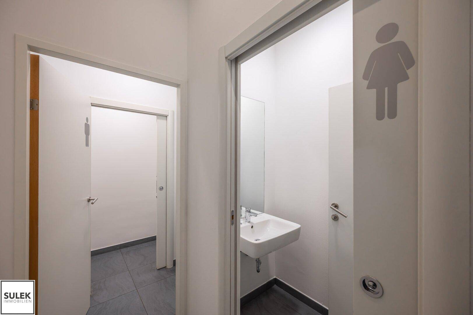 Moderne Toilettenräume mit Waschbecken und Spiegel, getrennt für Damen und Herren, in hellem Design.
