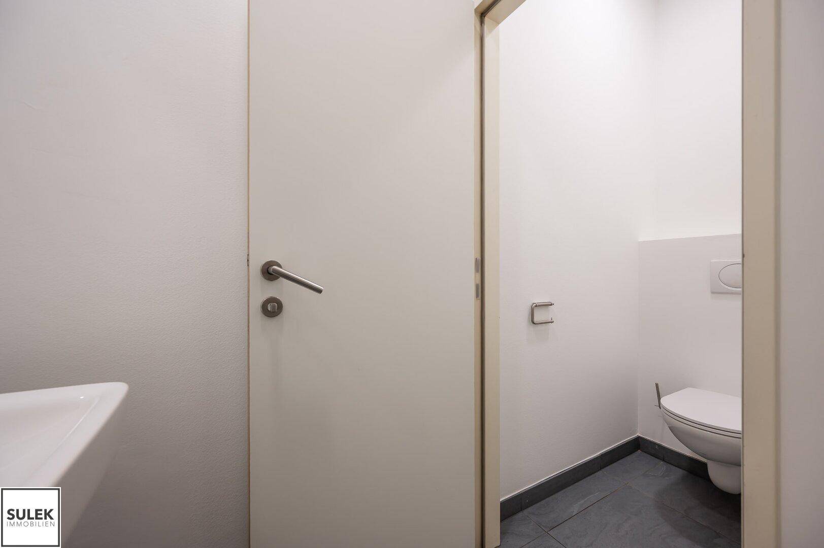 Saubere Toilette mit Wand-WC und Waschbecken, in einem hellen und funktionalen Design gehalten.