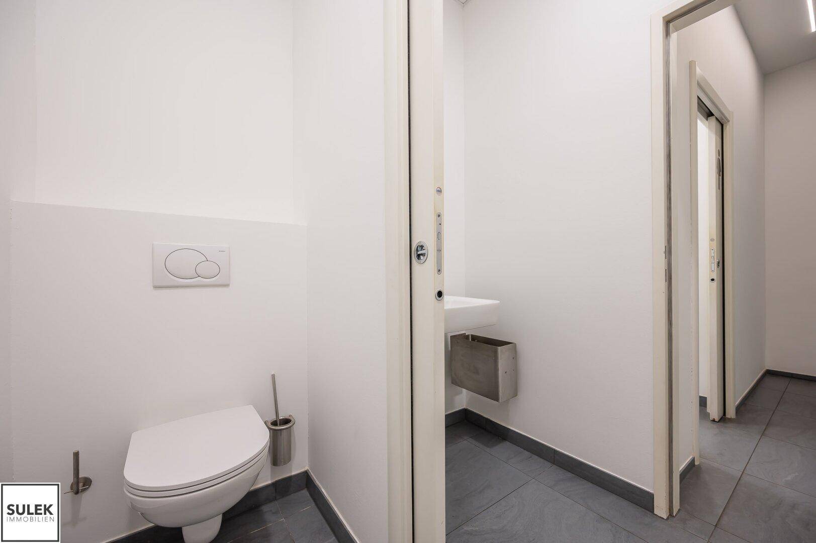 Saubere Toilette mit Wand-WC und Waschbecken, in einem hellen und funktionalen Design gehalten.